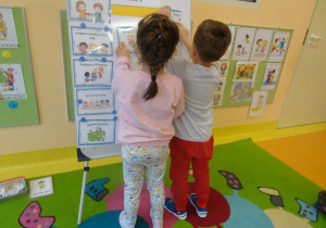 Dwójka dzieci zawiesza na tablicy zasady z Kodeksu dobrych relacji.